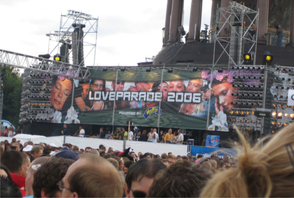 Hinter einer Menschenmenge leuchtet die Aufschrift "Loveparade 2006" auf einem Display
