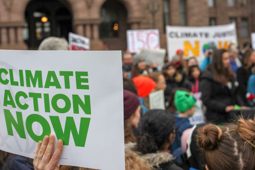 Demonstrant*innen von Fraidays for Future halten Schilder in die Luft. Auf einem im Vordergrund steht "Climate Action Now".