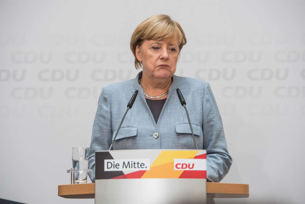 Angela Merkel steht vor einem Rednerpult, der mit dem Slogan "Die Mitte." und dem CDU-Logo beschriftet ist.